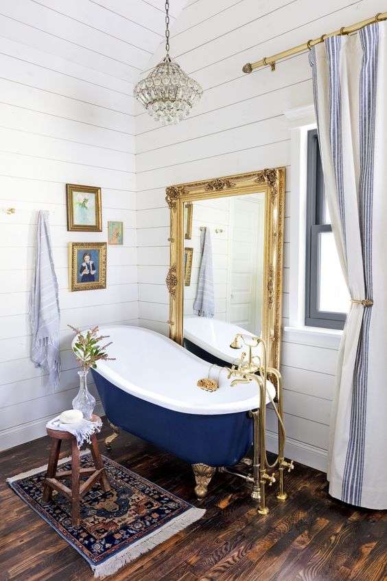دکوراسیون حمام با دیوارپوش سفید، کفپوش چوبی تیره، آینه‌ای در قاب طلایی پرآذین