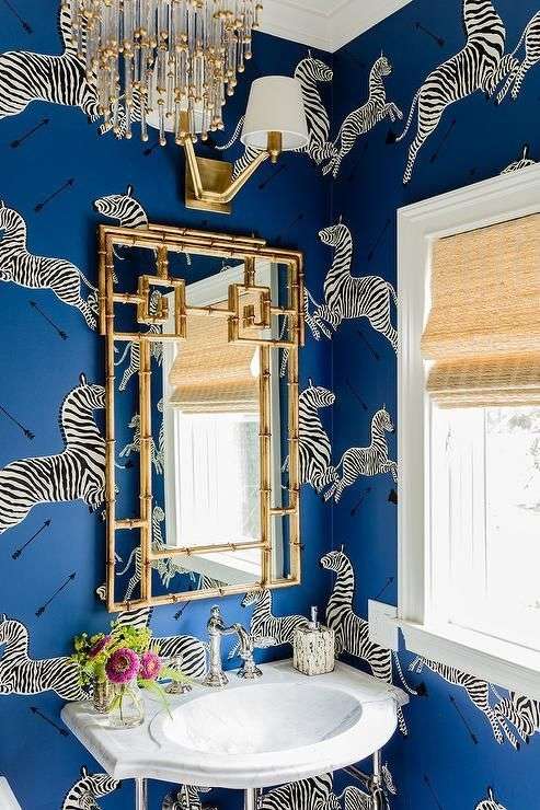 دکوراسیون یک دستشویی جالب توجه با کاغذ دیواری آبی با طرح گورخر، لوستر جذاب و یک قاب آینه طلایی که ترکیب مجموع اینها بسیار جسورانه به نظر می‌رسد.