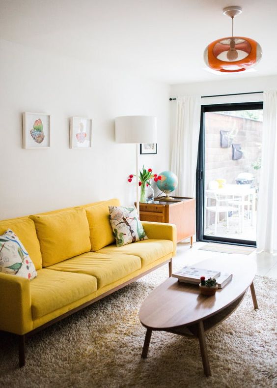 اتاق نشیمن کوچک و شاد با مبل زرد رنگ، میز بیضی شکل کم، یک دیوار گالری کوچک و یک چراغ روشن